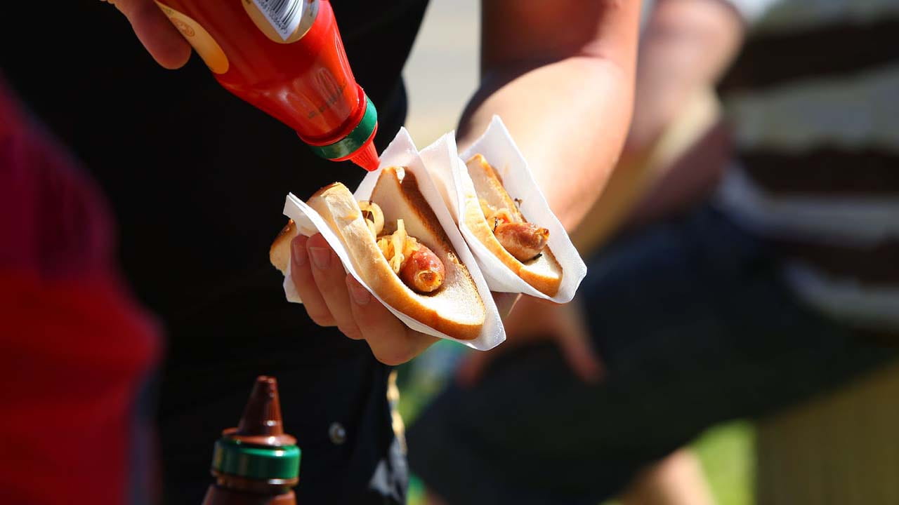 Squeezing tomato sauce on a hotdog wrapped in bread